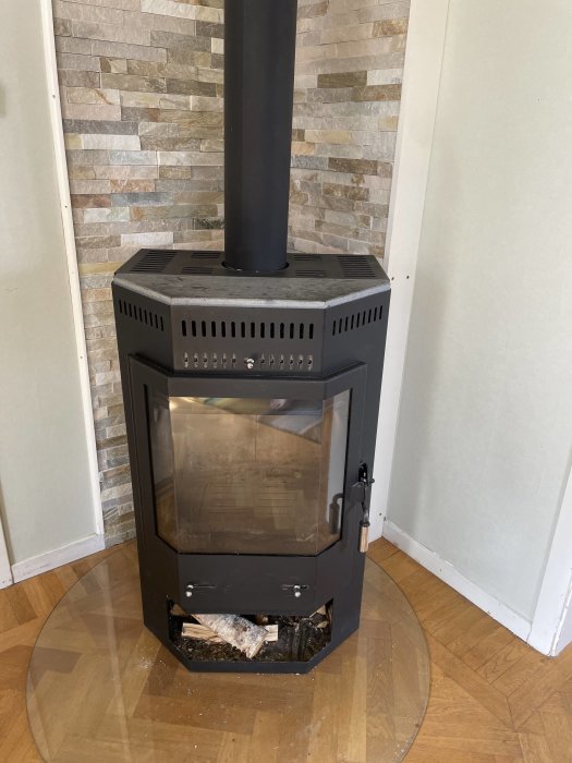 Svart hörnplacering kamin med glasdörr och ved, utan synliga märken, installeras i rum med tegelvägg.