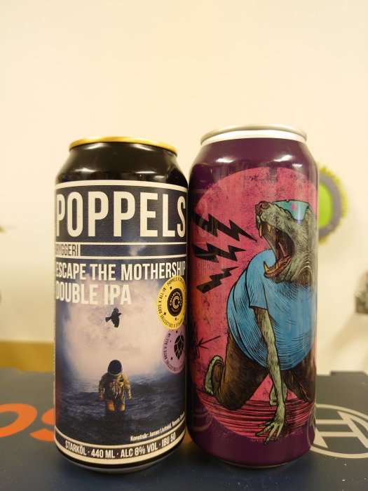 Två ölburkar, en med motiv på en astronaut och texten "ESCAPE THE MOTHERSHIP DOUBLE IPA", den andra med en dansande björn.