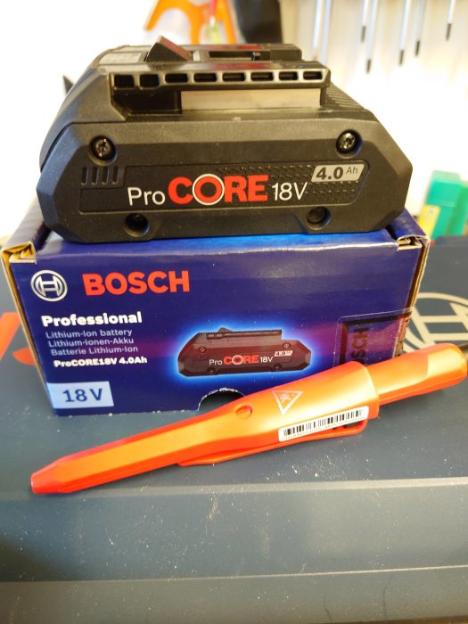 Bosch ProCORE 18V 4.0Ah batteri ovanpå förpackningen bredvid en röd snickarpenna på ett arbetsbord.