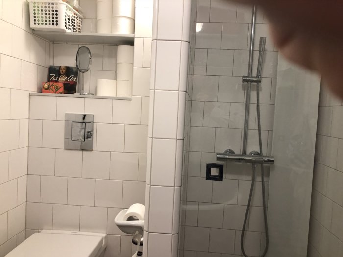 Ett litet, effektivt inrett badrum med dusch, toalett och hyllor för förvaring.