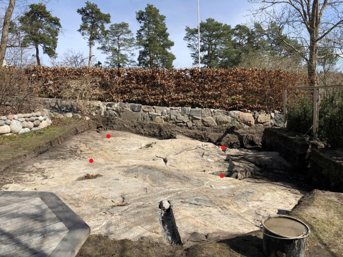 Ojämn berggrund med röda markeringar för planering av växthusgrund.