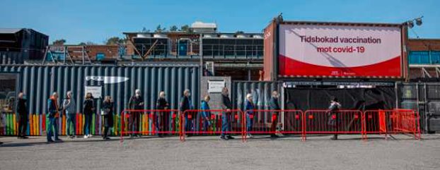 Människor i kö med varierande avstånd utanför vaccinationscenter för covid-19.