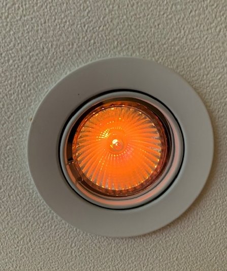 Närbild på en tänd halogen spotlight med orange sken infälld i vitt tak.