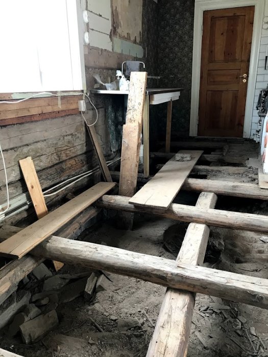 Rivet golv i ett timmerhus med synliga bjälkar och temporära brädor över bjälklaget.