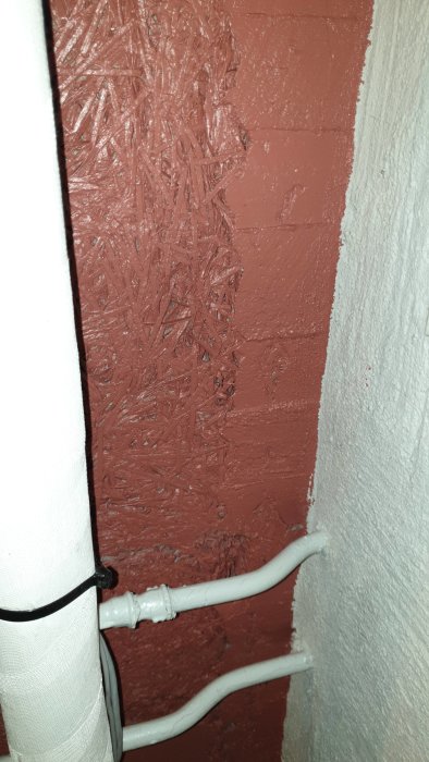 Fiberplattor på vägg i oljerum, delvis täckta med röd sprayfärg och putslager som släppt, med synliga rörledningar.