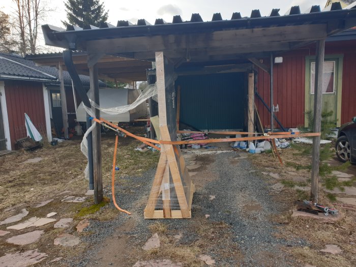 Delvis byggd carport med trästomme och oavslutat tak vid rödfärgat hus.