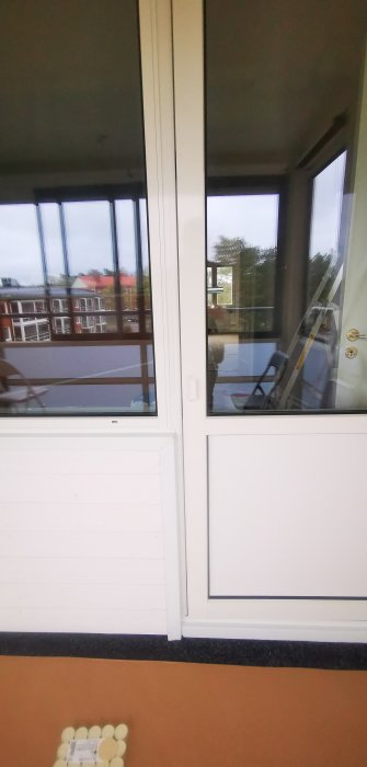 Utsikt från insidan av en inglasad balkong med en stängd vit dörr utan lås från utsidan.