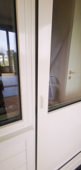 Vit balkongdörr med handtag och utan synligt lås, öppnad inåt mot en inglasad balkong.