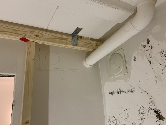 Avloppsrör längs taket i ett hörn av ett rått källarrum med anmärkningsskisser på väggen samt synlig isolering.