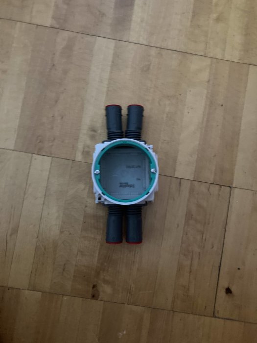 Elektrisk kopplingsdosa med två sladdar och avtagbara sidostycken på trägolv.