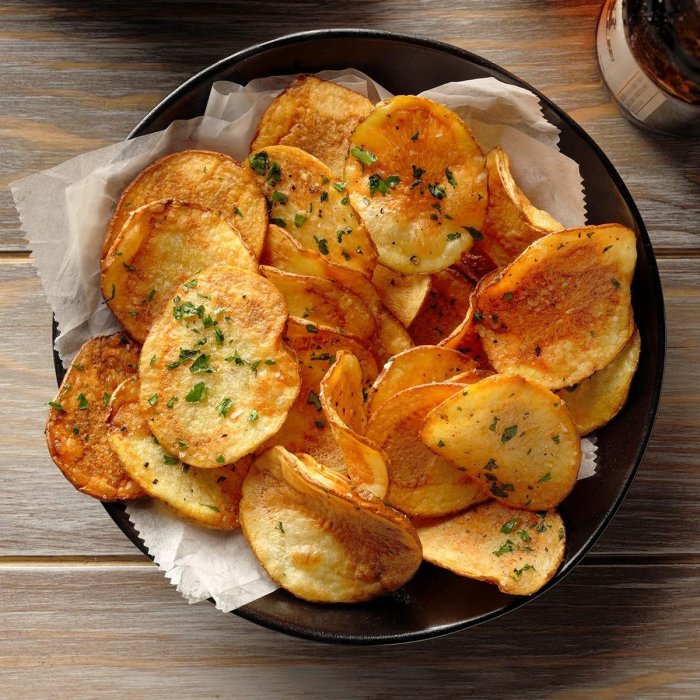 Hembakade kryddiga potatischips i en svart skål på ett träbord.