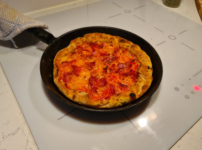 Hemlagad pizza i gjutjärnspanna på spishäll.