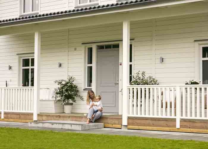 Två personer sitter på trappan till ett hus med veranda och tak, entrédörren i mitten.