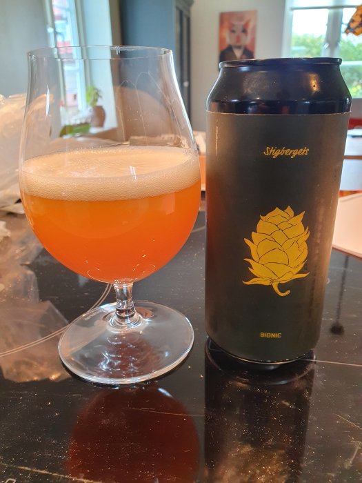 Fylligt orange IPA-öl i ett glas bredvid en mörk ölburk med humletryck.