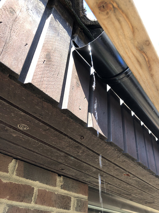 Nyinstallerad hängränna längs takkanten med synliga krokar och stuprör mot trävägg och tegelsten.