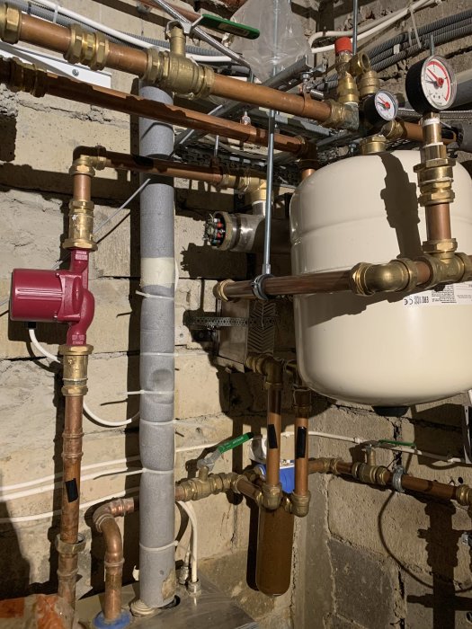 Värmesystem med kopparledningar, pump, expansionskärl och mätinstrument i ett pannrum.