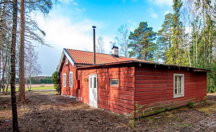 Röd trästuga med platt tak och synlig utbyggnad i naturskön miljö.