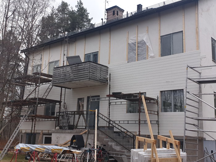 Renovering av husfasad med ställningar och omonterade fönster på marken.