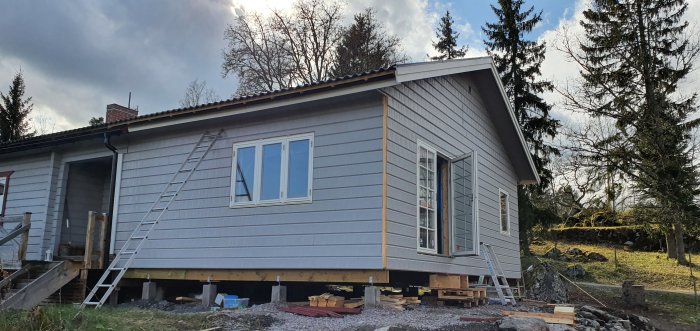 Nyinstallerade fönster och dörrar på ett hus under renovering, med en stege på sidan.