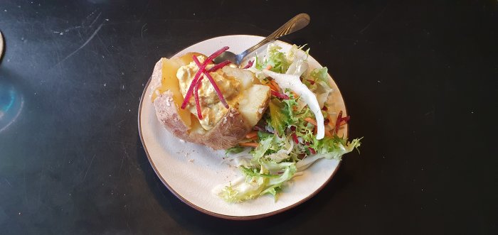 Bakad potatis med räkröra och grönsallad på en beige tallrik mot en svart bakgrund.