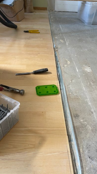 Skarv mellan askgolv och betonggolv med verktyg och skruvar på golvet.