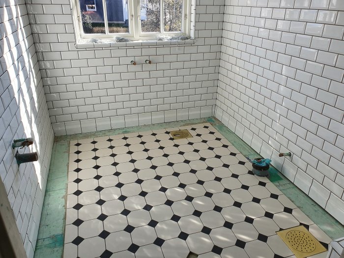 Nyinstallerat svartvitt hexagonalt kakelgolv i ett rum med vita subway-tiles på väggarna, redo för frisinstallation.