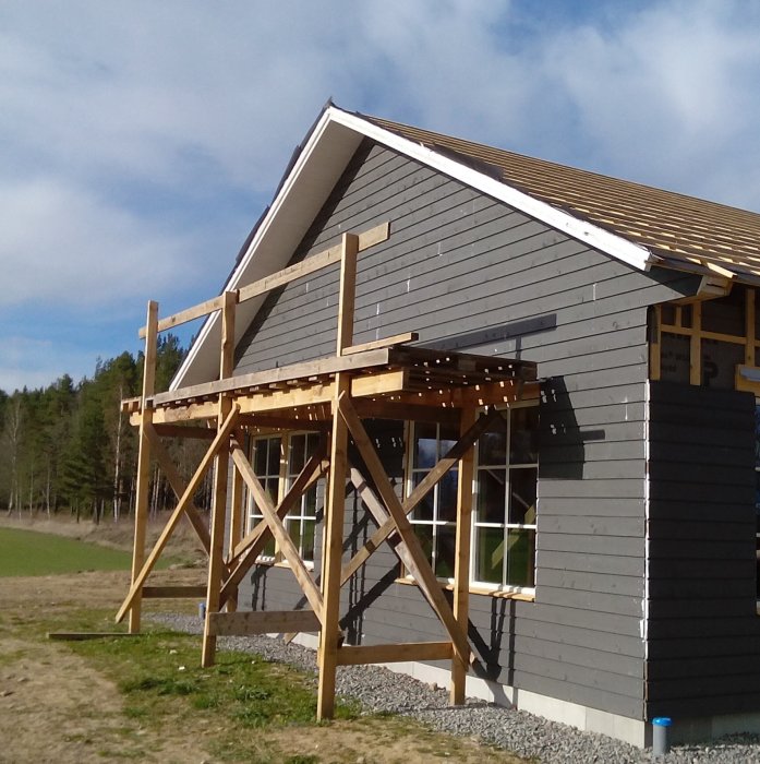 Träställning monterad på sidan av ett hus under konstruktion med synlig trästomme och grå ytterpanel.