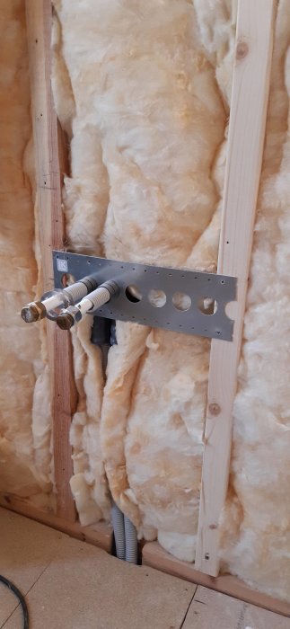 Installationsplåt för PEX-rör monterad på träregel med isolering i bakgrunden.