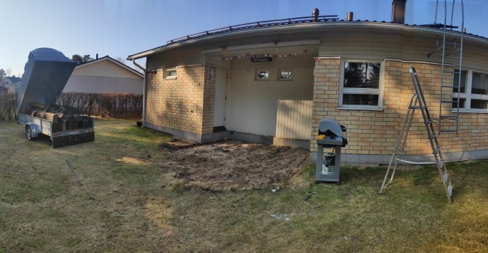 Tom yta vid husvägg där slipers har tagits bort, släpvagn med byggmaterial och stege vid sidan.