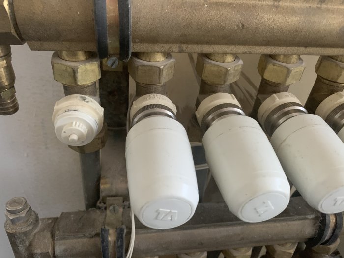 Vit ventilpiggen på en vattenburen golvvärmesystemsventil som har kärvat fast, visas bredvid andra termostatventiler.