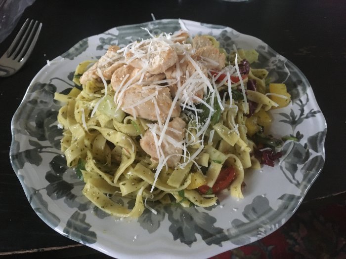 Pastasallad med pesto, kyckling och riven parmesan på en blommig tallrik.