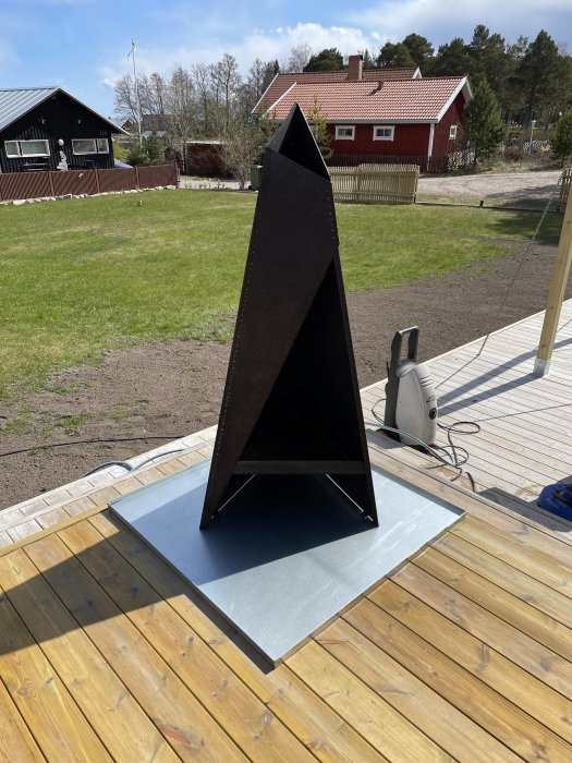 Nyinstallerad kamin på silverfärgat underlägg på trätrall med hus och gräsmatta i bakgrunden.