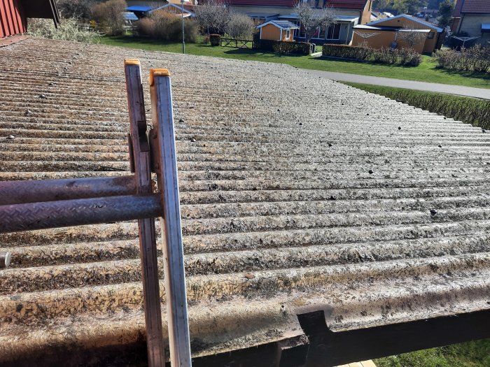 Rivet gammalt tak med träkonstruktion och en pergola under uppbyggnad, med en trädgård och hus i bakgrunden.