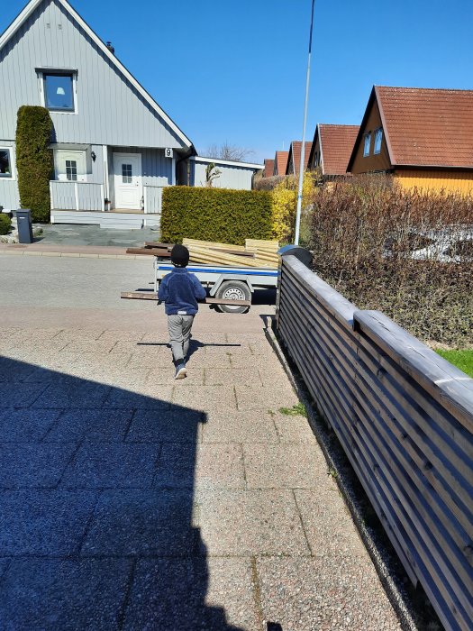 Barn hjälper till att bära virke till en blivande pergola vid en bostad på en solig dag.