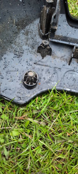 Del av en svart plastkomponent med magnetisk fästelement liggande på fuktigt gräs.