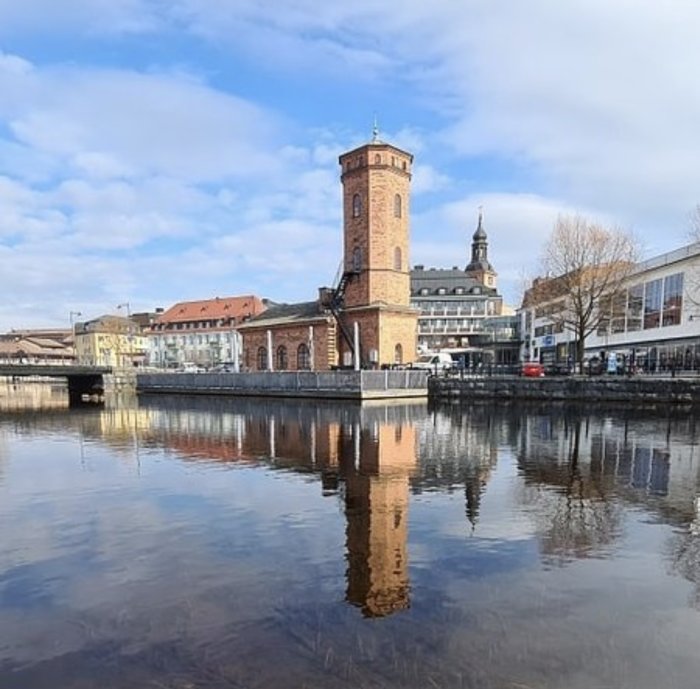 Historisk byggnad vid vatten i Falun, tidigare Villovägens bryggeri, med spegling i vattnet och klar himmel.