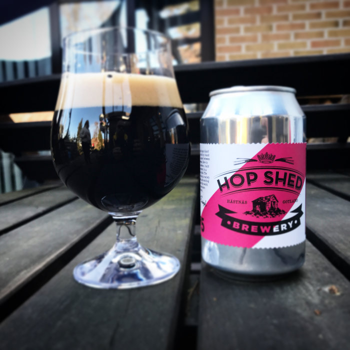 Ett glas mörk porter och en burk från Hop Shed Brewery på ett utebord.