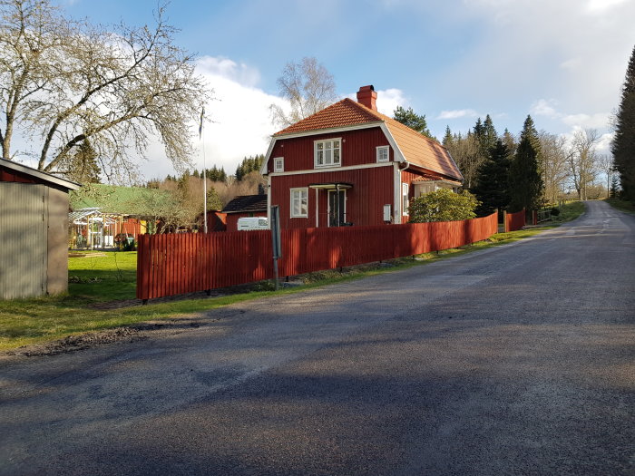 Nyligen färdigställt rött staket vid ett rödmålat hus med omgivande grönska.