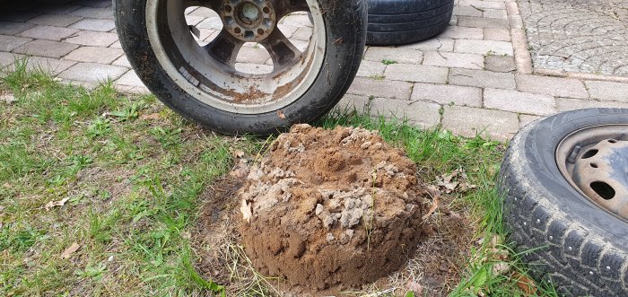 Stor jordhög bredvid två gamla bildäck på gräs och stenplattor, liknar en "sandtårta".