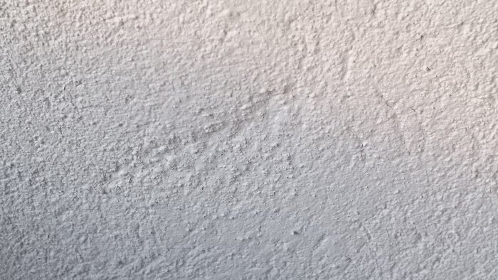 Grov overflade på en hvidmalet væg med ujævn pudset tekstur og synlige huller.