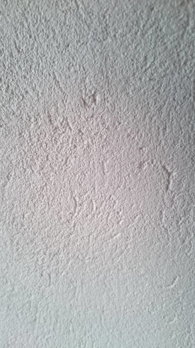 Grov og ujævn væg overflade med riller og fordybninger, tydeligt når sollys rammer; slidte, delvist udførte pusningsforsøg.