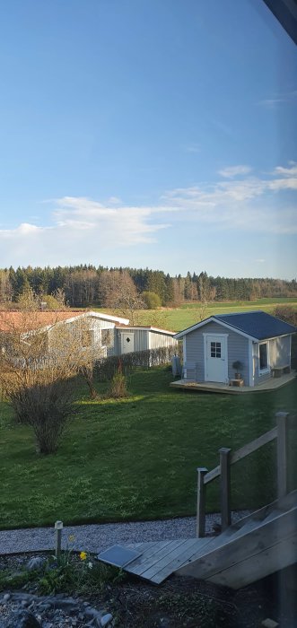 Utsikt från ett sovrum med äng och skog i bakgrunden, gräsmatta och en friggebod i förgrunden.