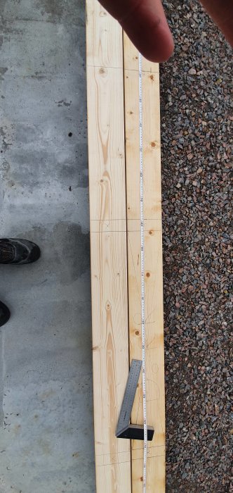 Mätning av träsyll med tumstock och vinkelhake, markerade kapningspunkter, sten och betongunderlag.