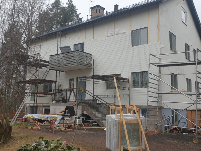 Hus under renovering med nya vita panelbrädor, byggställning och omonterade paneler på marken.