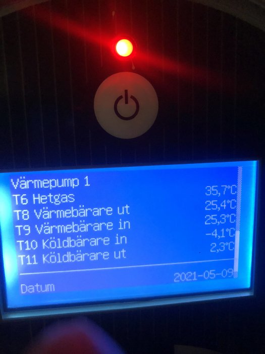 Värmepumpens display visar temperaturvärden och status med en röd lampa ovanför.