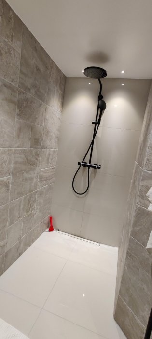 Modern duschhörna med stora kakelplattor, svart duschset och infälld belysning.
