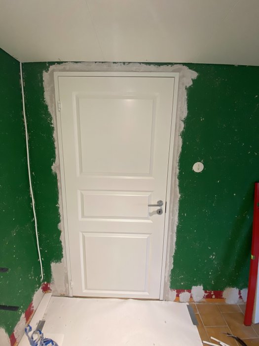 Vit dörr med nyspacklade kanter runt karmen mot en grön vägg under renovering.