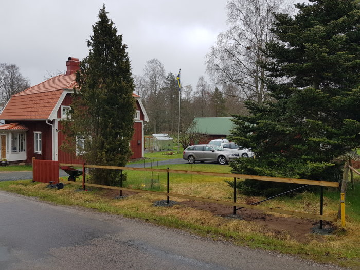 Nymonterade träspjälor på en staketgrund med hus och bil i bakgrunden en regnig dag.