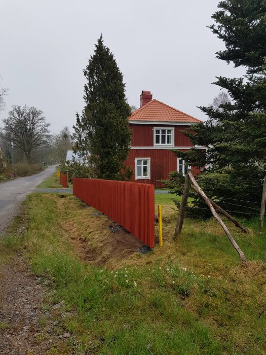 Nyuppsatta röda staketspjälor vid en röd stuga under en mulen himmel.