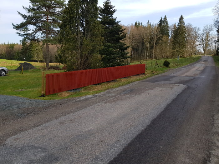 Nymålat rött staket längs en landsväg med nyuppskruvade staketspjälor.